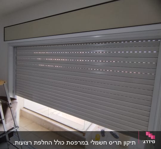 תריס גלילה אפור בחלון גדול עם מסגרת לבנה